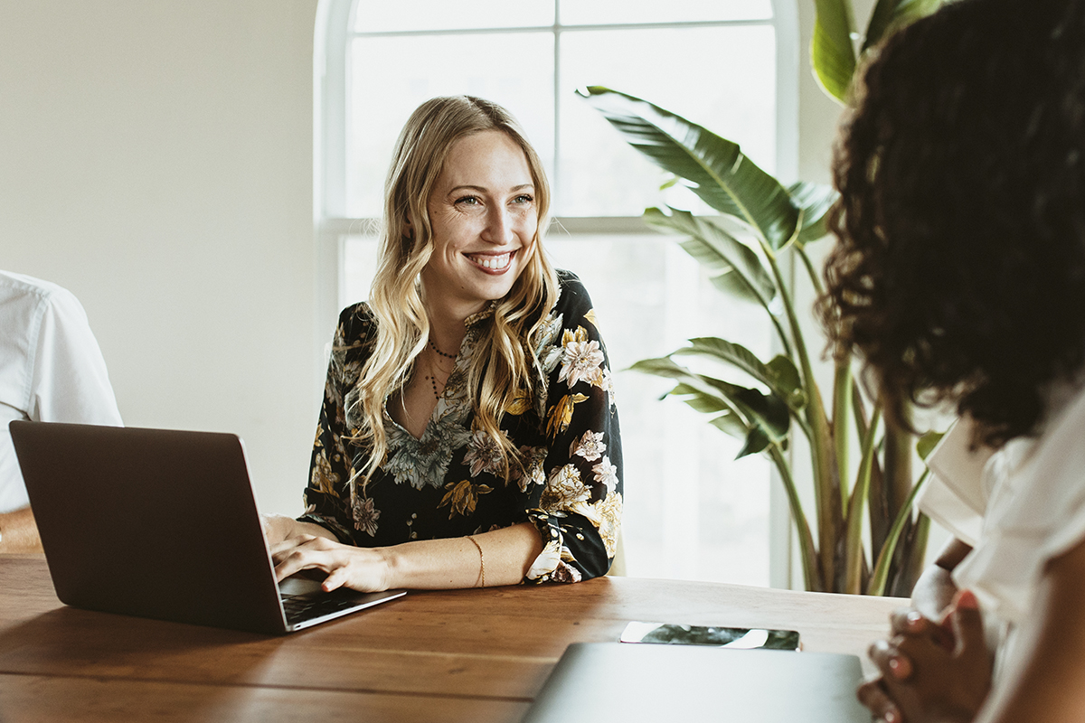 Woman sitting at computer and smiling at another woman