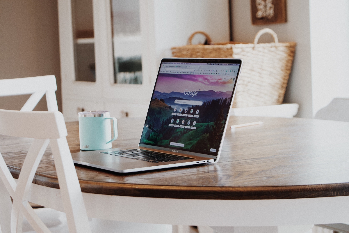 A laptop on a wooden dining table displaying the Google homepage, representing the comparison between Outlook and Google for productivity and email management.