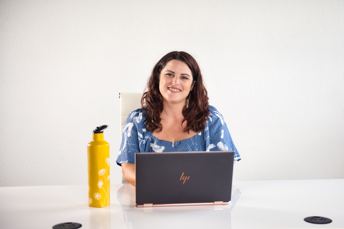 A smiling woman sitting at a desk with a laptop, representing effective virtual communication and the use of away messages for professional workflow.