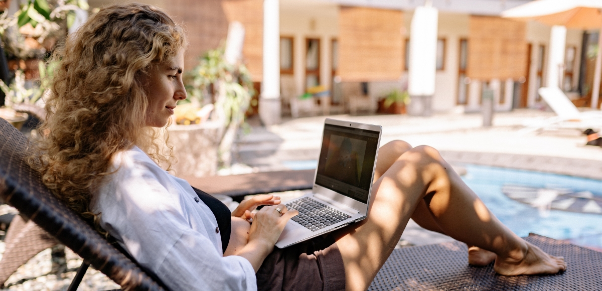 A woman working on her laptop while relaxing on a lounge chair by the pool, enjoying a balance between work and fun.