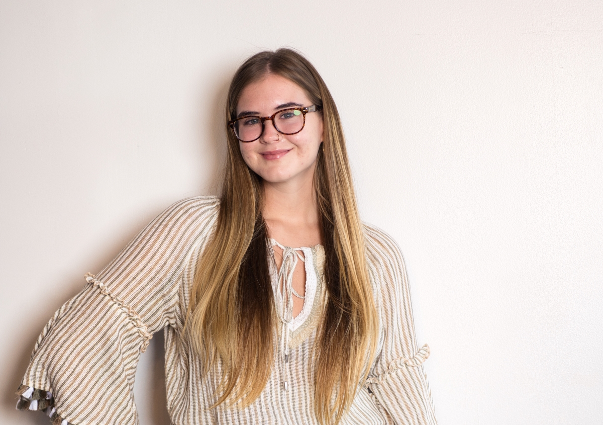 A young woman with long hair and glasses smiling confidently, symbolizing self-expression and finding your voice.