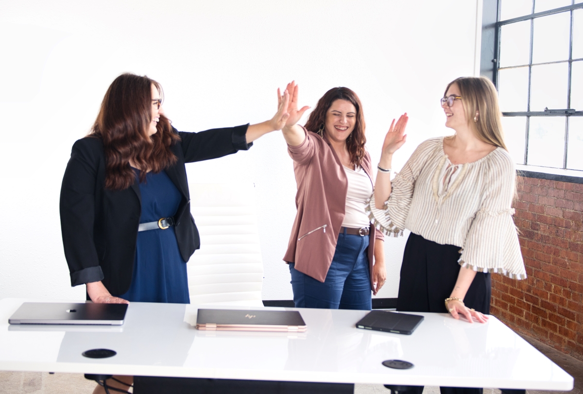 Three women giving each other high fives in an office setting, demonstrating appreciation and teamwork in the workplace.