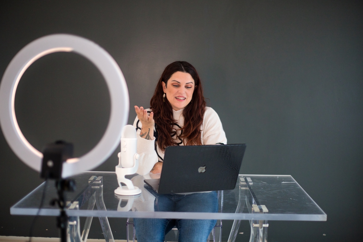 A woman conducting a virtual meeting with a laptop, microphone, and ring light, focused on managing client expectations effectively.