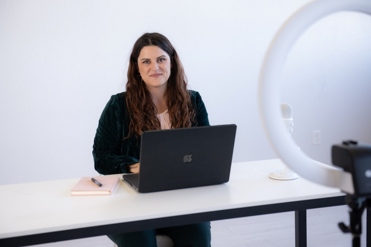 A professional woman with a laptop sitting at a desk, ready for a virtual meeting, with a ring light and microphone setup.