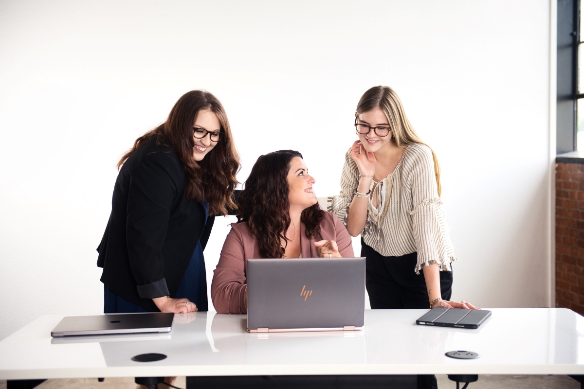 A group of three women collaborating at a desk, focused on a laptop, working together to achieve business goals.