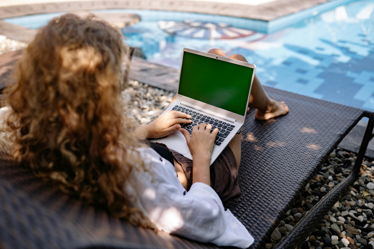 Woman working on a laptop by the pool during summer.