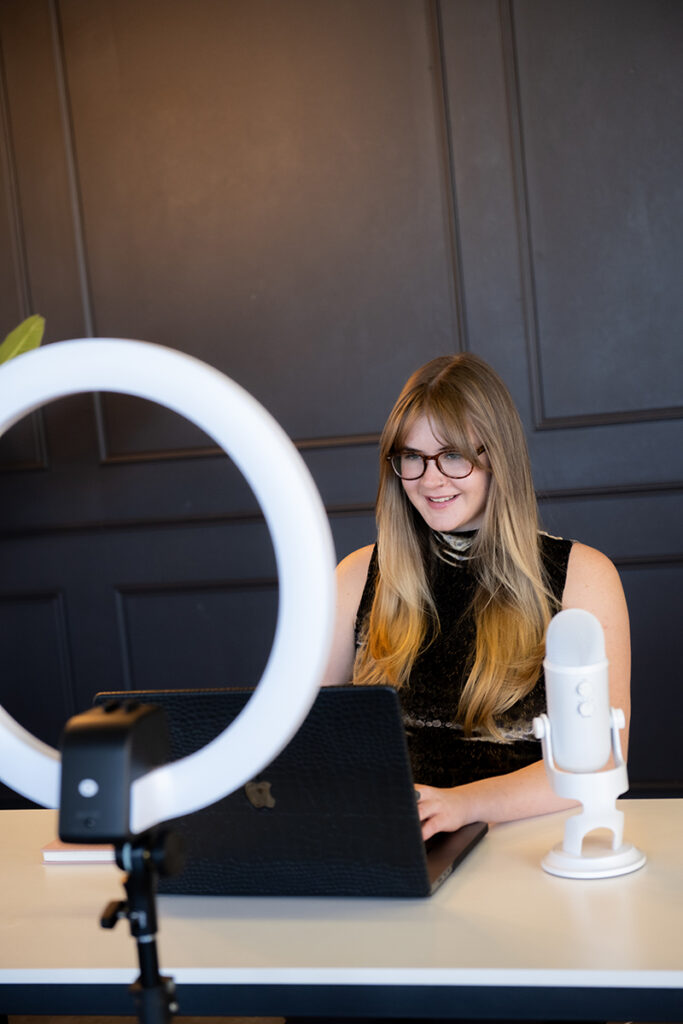 A virtual assistant from a professional agency working on a laptop, equipped with a microphone and ring light for a virtual meeting.