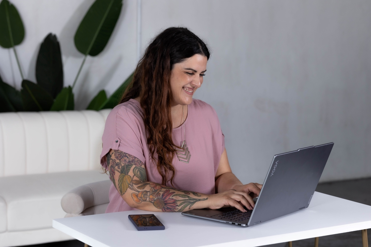 A smiling woman working on a laptop in a modern workspace, symbolizing structured workflows and SOPs creation.