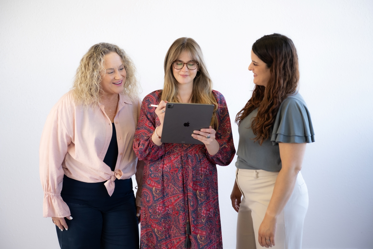 Three women collaborating on holiday marketing strategies using a tablet.