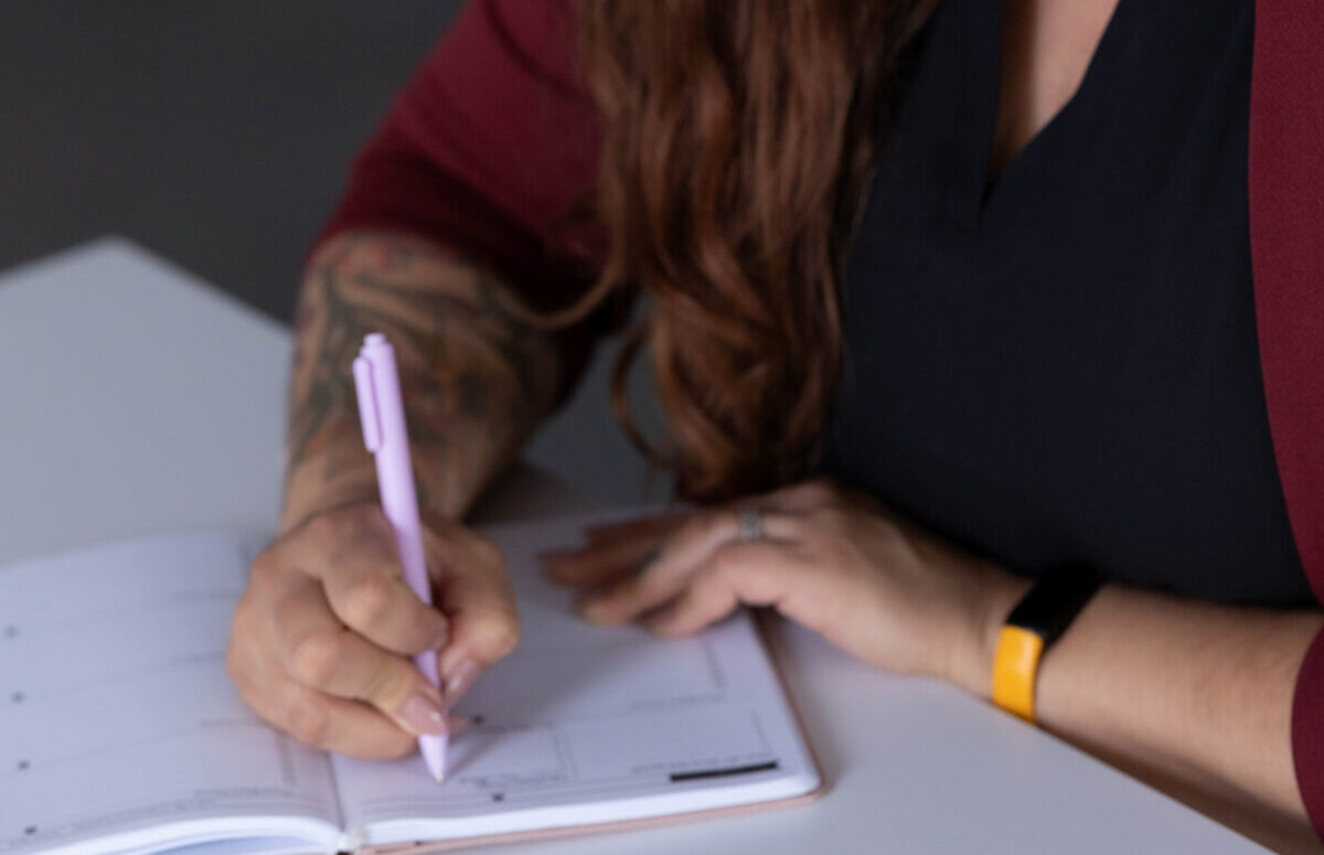 A professional woman writing in a planner, documenting SOP onboarding steps.