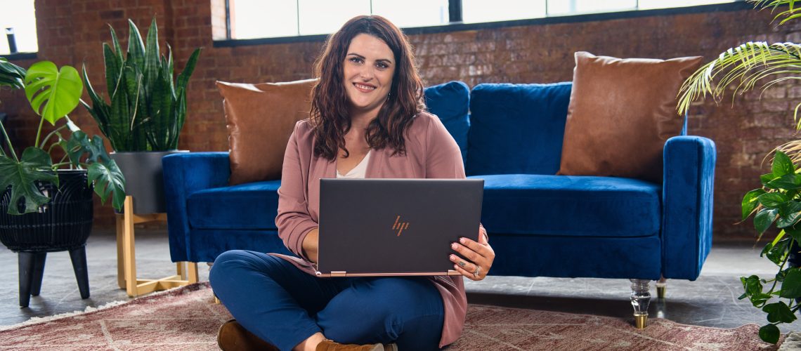 happy-woman-sitting-on-floor-on-laptop-smiling-at-camera