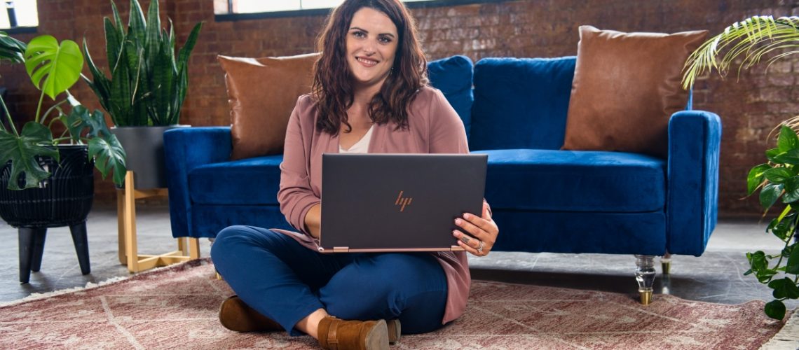 A smiling woman sitting on the floor with a laptop in a stylish, cozy workspace, representing productivity and time management.
