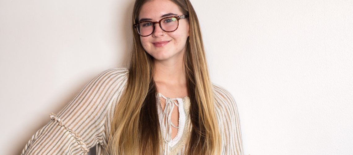 A young woman with long hair and glasses smiling confidently, symbolizing self-expression and finding your voice.