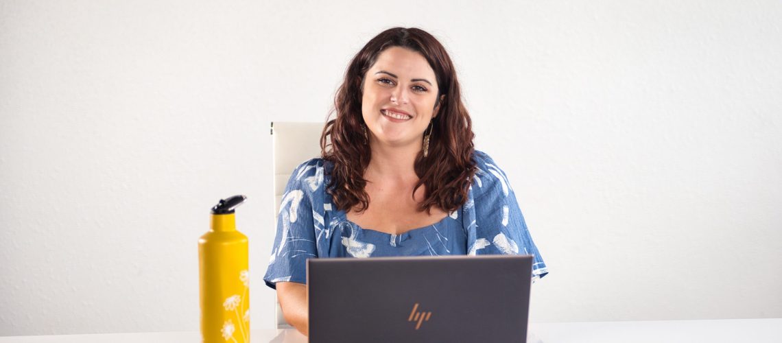 business-woman-sitting-at-laptop-with-yellow-water-bottle-in-blue-spring-dress