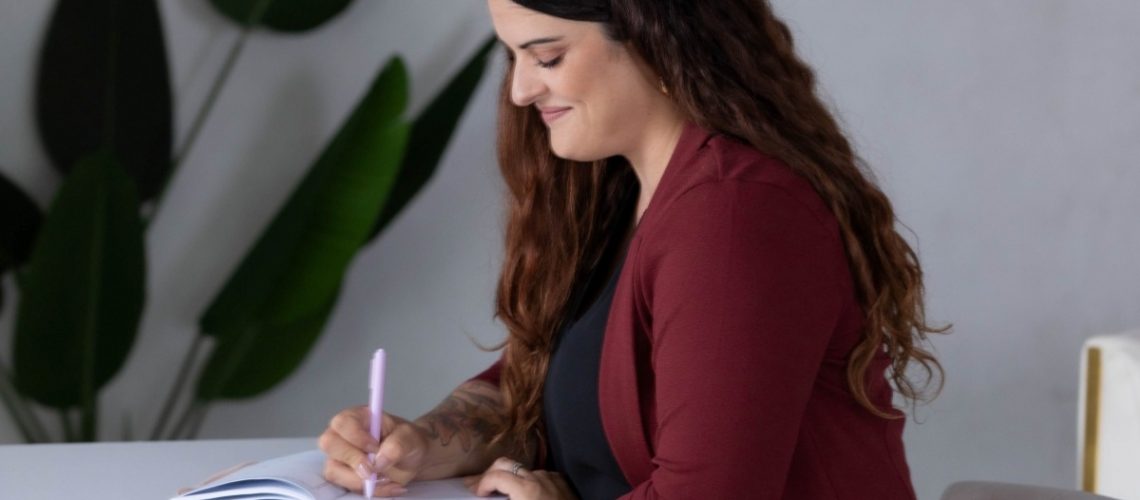 Professional woman sitting down at desk writing out real examples of process optimization.