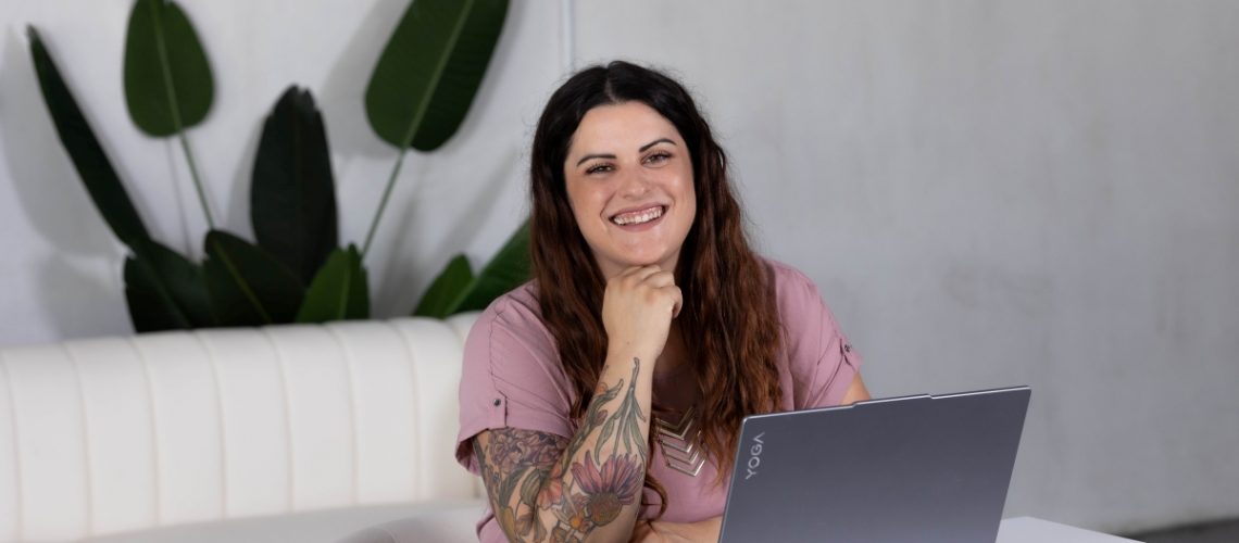 Smiling woman sitting at a desk with a laptop, representing a professional virtual assistant available for hire.