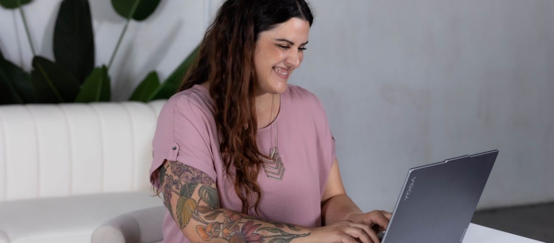 A smiling woman working on a laptop in a modern workspace, symbolizing structured workflows and SOPs creation.