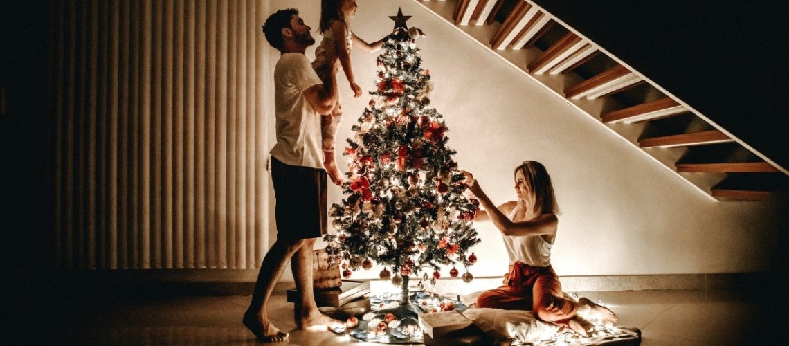 A family decorating a Christmas tree together in a cozy, dimly lit home during the holiday season.
