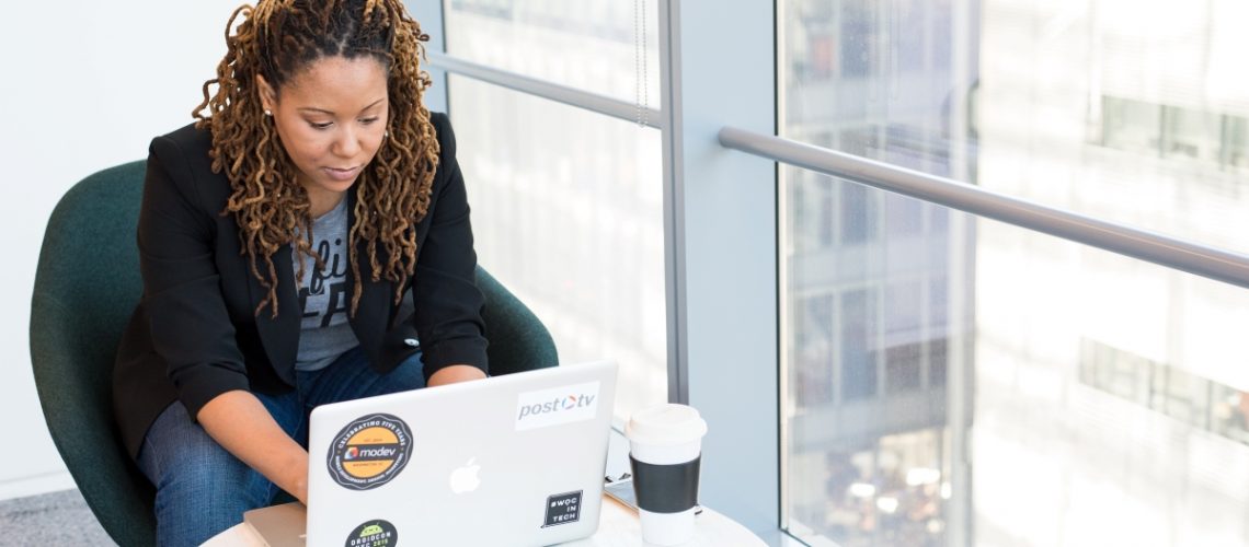 A professional woman working on her laptop in a modern office with a city view, managing her schedule efficiently.
