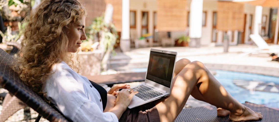 woman-sitting-outside-working-on-laptop-with-kid-poolside