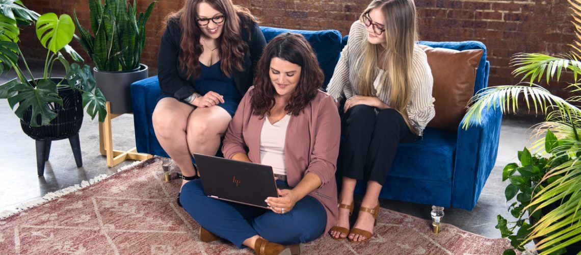 Three professional women working together on a laptop in a stylish office setting, focused on setting themselves up for success.